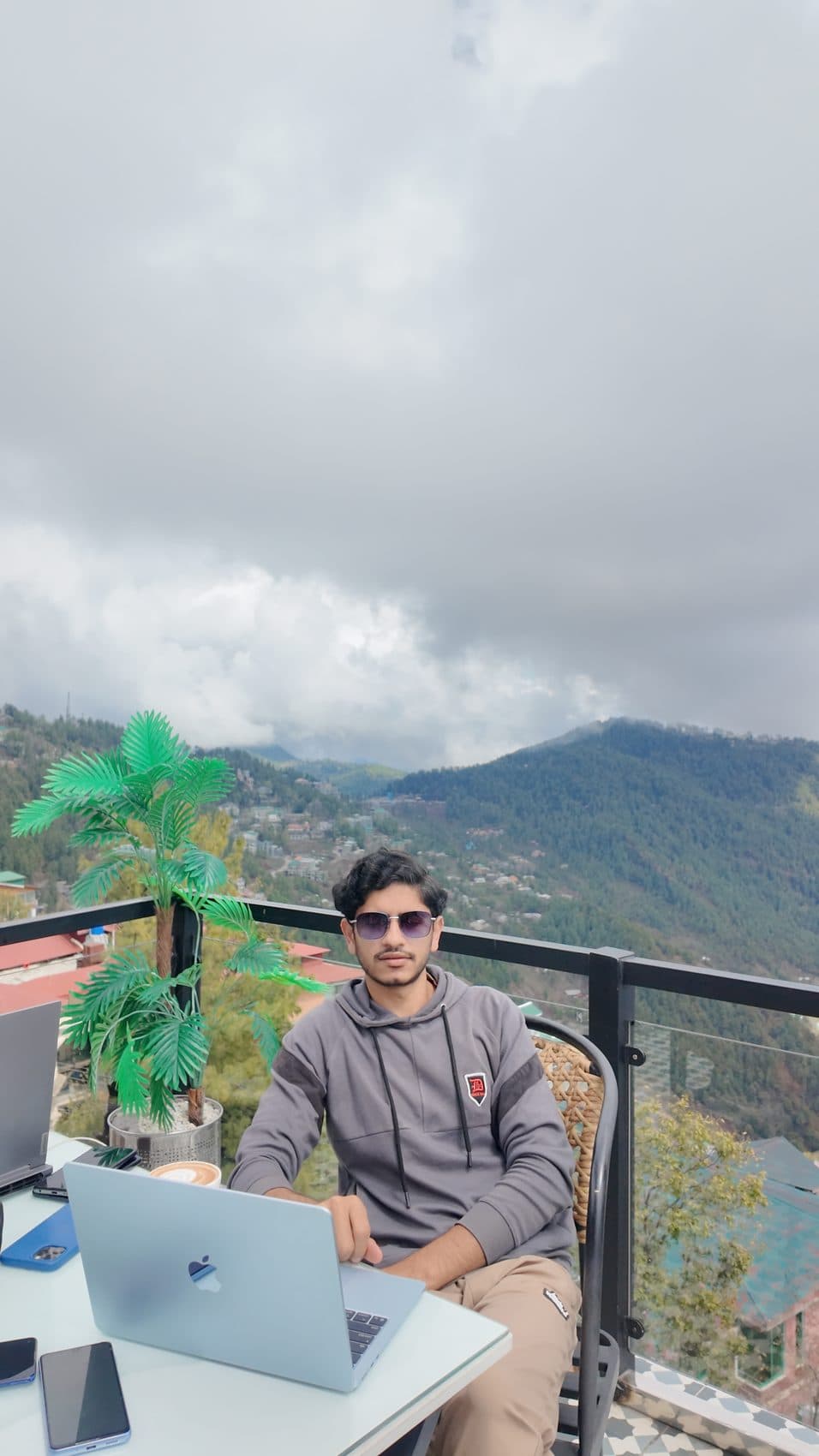 Waseem working on a laptop at a rooftop cafe above mountain clouds
